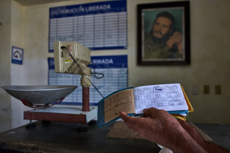 Un hombre muestra su libreta de racionamiento, mientras al fondo se ve una imagen enmarcada de Fidel Castro, en una tienda estatal en La Habana, Cuba. (Foto: AP/Ramón Espinosa)