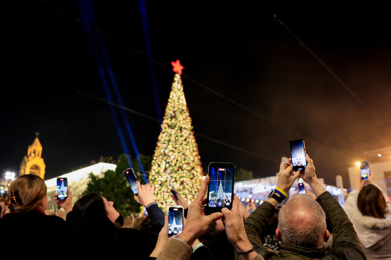 Palestinos usan teléfonos para grabar mientras se enciende un árbol de Navidad en la Plaza del Pesebre, afuera de la Iglesia de la Natividad, en Belén, Cisjordania ocupada por Israel, el 6 de diciembre de 2025. REUTERS/Mussa Qawasma